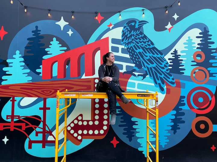 a woman sitting on a scaffolding in front of a mural